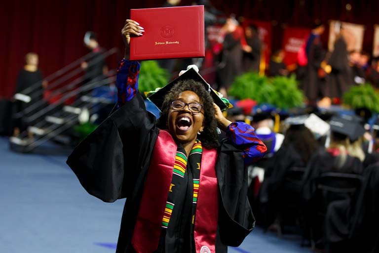 an IU South Bend graduate holds her IU degree high in the air.